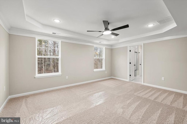 empty room featuring light colored carpet, a tray ceiling, visible vents, and baseboards