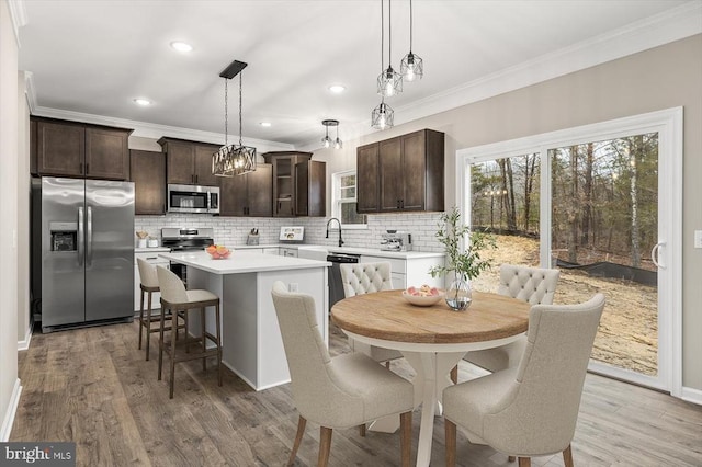 kitchen with dark brown cabinetry, stainless steel appliances, hanging light fixtures, light countertops, and a center island