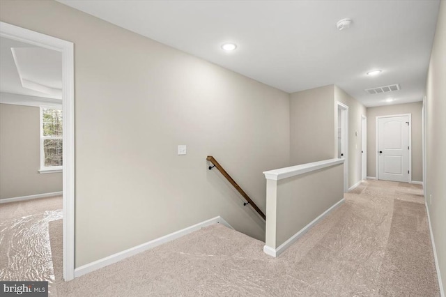 hallway featuring baseboards, visible vents, light carpet, and an upstairs landing