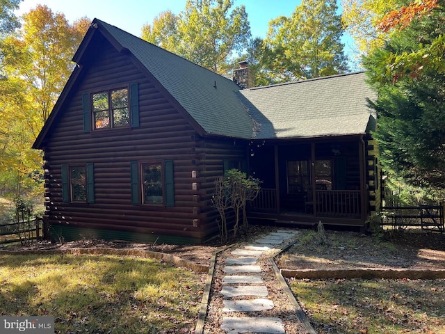 cabin featuring a sunroom, a chimney, log siding, and fence