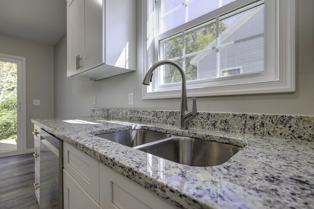 kitchen featuring light stone counters, dishwasher, sink, and white cabinets