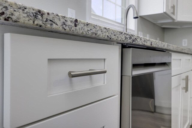 interior details with dishwasher, light stone countertops, and white cabinets