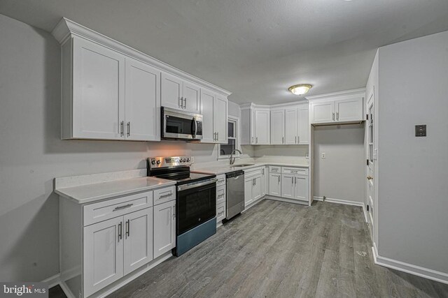 kitchen featuring white cabinetry, stainless steel appliances, sink, and light hardwood / wood-style flooring