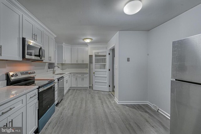 kitchen with appliances with stainless steel finishes, sink, white cabinets, and light hardwood / wood-style floors