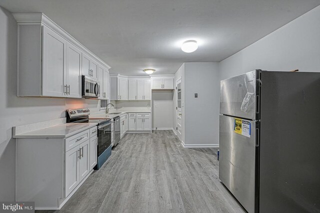 kitchen with white cabinetry, stainless steel appliances, sink, and light hardwood / wood-style flooring