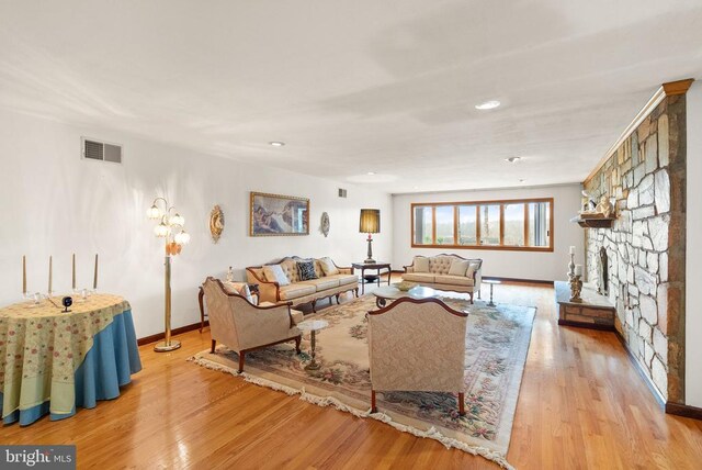 living room featuring baseboards, a fireplace, visible vents, and wood finished floors