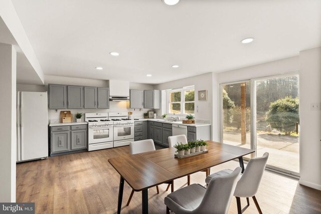 kitchen with gray cabinets, light countertops, light wood-style floors, white appliances, and under cabinet range hood