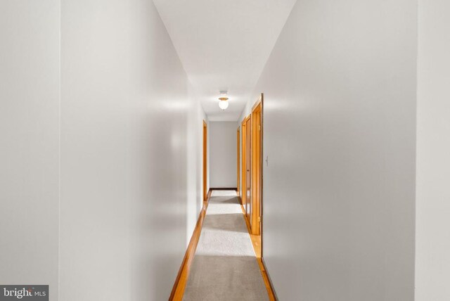 hallway featuring light carpet and baseboards