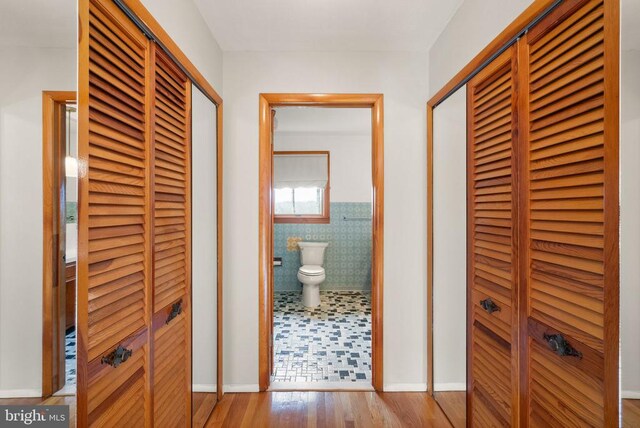 hallway featuring wainscoting, wood finished floors, and tile walls