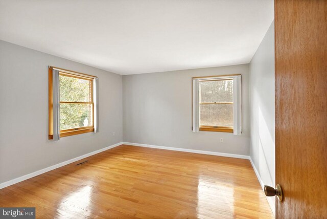 spare room featuring light wood-style floors, visible vents, and baseboards