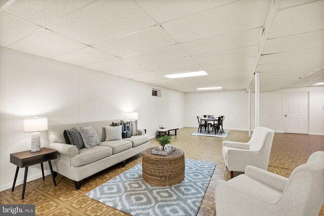 living area with a paneled ceiling and baseboards