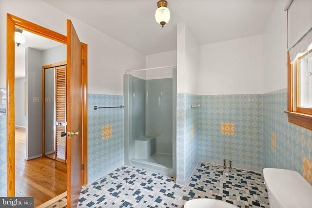 bathroom with toilet, a stall shower, tile walls, and a wainscoted wall