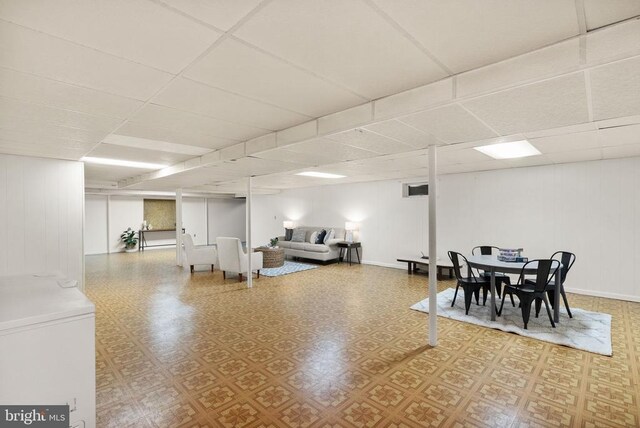 finished below grade area with fridge, baseboards, a drop ceiling, and tile patterned floors