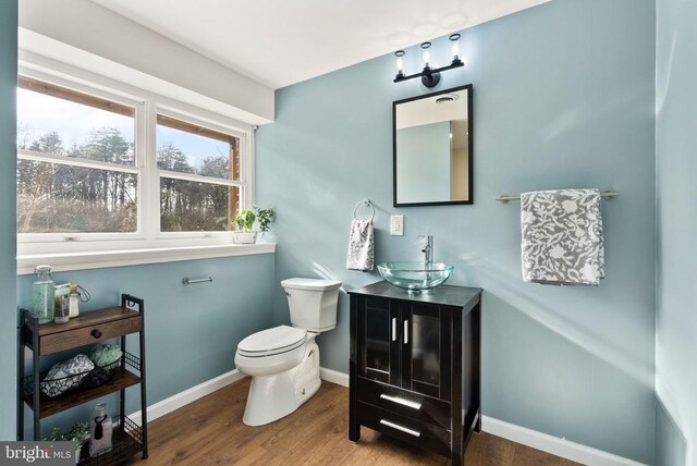 half bathroom with vanity, wood finished floors, toilet, and baseboards