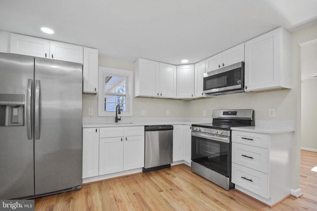 kitchen with stainless steel appliances, white cabinetry, sink, and light hardwood / wood-style flooring