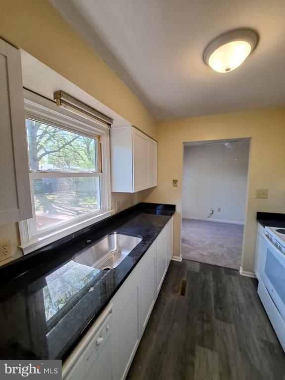 kitchen featuring dark countertops, dark wood-type flooring, white cabinets, white appliances, and baseboards