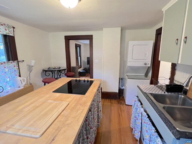 kitchen featuring sink, wooden counters, stacked washing maching and dryer, black electric stovetop, and light hardwood / wood-style floors