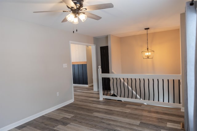 empty room with ceiling fan with notable chandelier, baseboards, and wood finished floors