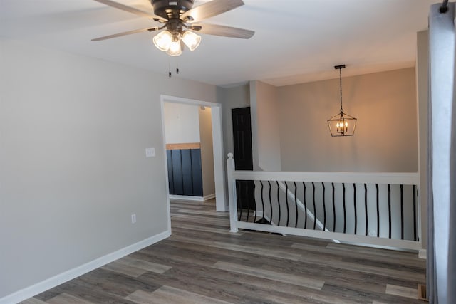 empty room featuring ceiling fan with notable chandelier, wood finished floors, and baseboards