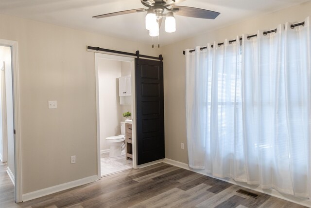 unfurnished bedroom with a barn door, connected bathroom, wood finished floors, visible vents, and baseboards