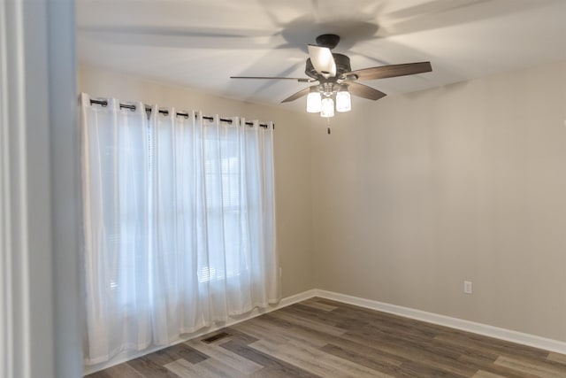 empty room with a ceiling fan, wood finished floors, visible vents, and baseboards