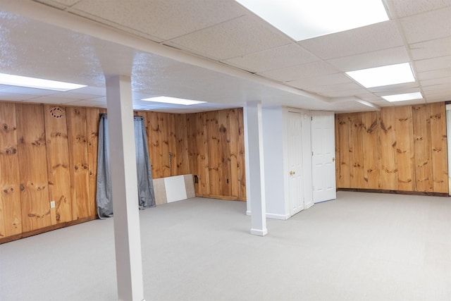 finished below grade area featuring light carpet, wooden walls, and a drop ceiling