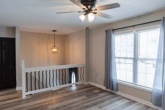 unfurnished room with an inviting chandelier, a healthy amount of sunlight, baseboards, and wood finished floors