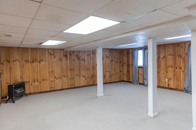 basement with wood walls, a paneled ceiling, and a wood stove