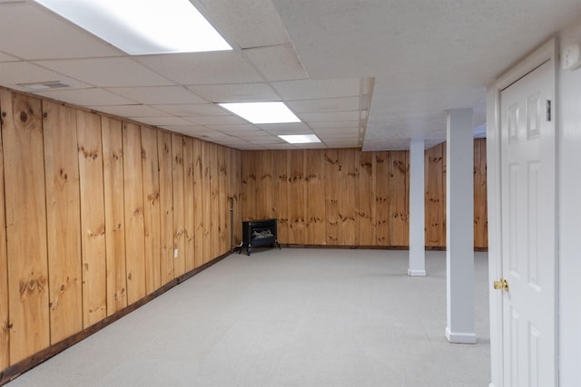 finished below grade area with a paneled ceiling, wood walls, baseboards, light floors, and a wood stove