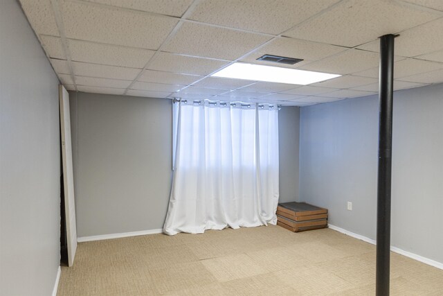 basement featuring a drop ceiling, wooden walls, and a wood stove