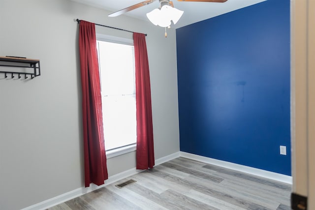 empty room with a ceiling fan, wood finished floors, visible vents, and baseboards