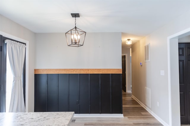 unfurnished dining area featuring light wood-type flooring, baseboards, visible vents, and a chandelier