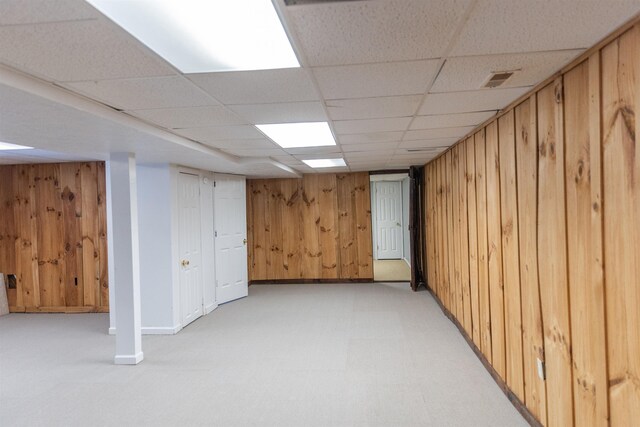 basement with a paneled ceiling, light colored carpet, and wood walls