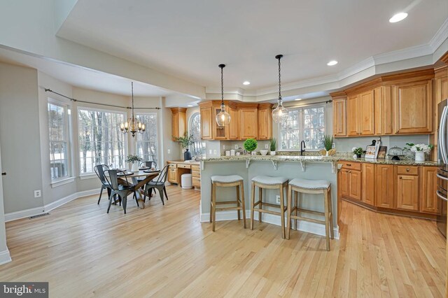 kitchen with a center island, hanging light fixtures, light hardwood / wood-style flooring, a kitchen breakfast bar, and light stone countertops