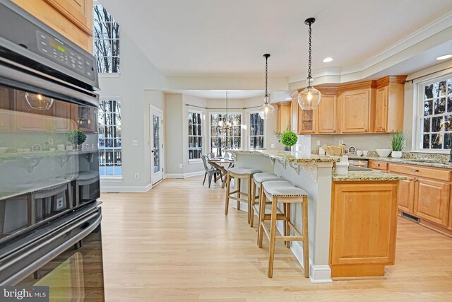 kitchen featuring a breakfast bar, a kitchen island, a notable chandelier, light stone countertops, and light hardwood / wood-style floors