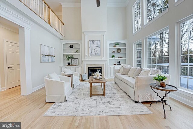 living room with a high ceiling, crown molding, built in features, and light hardwood / wood-style flooring