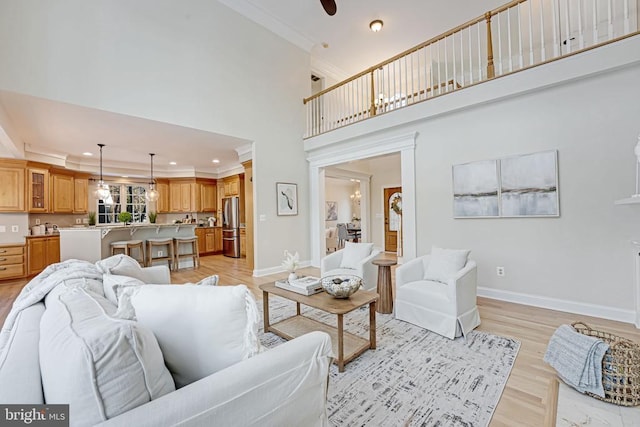 living room with ceiling fan, ornamental molding, a high ceiling, and light wood-type flooring