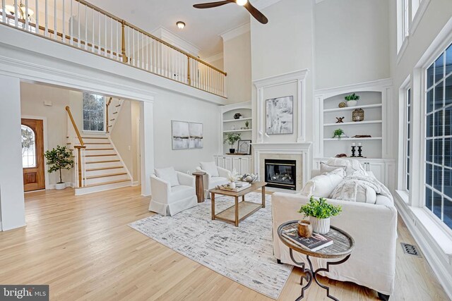 living room featuring ceiling fan, a high ceiling, ornamental molding, built in shelves, and light wood-type flooring