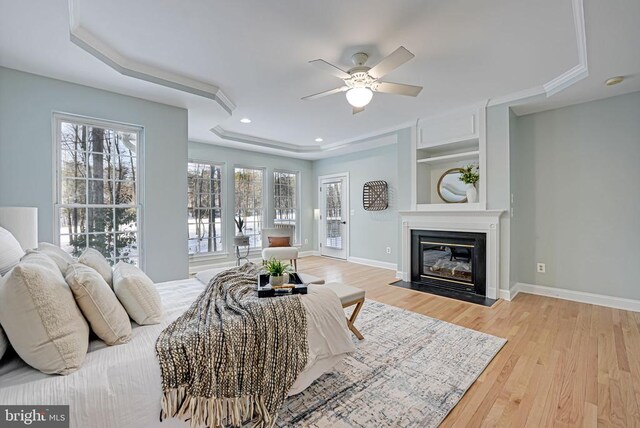 bedroom featuring access to outside, light hardwood / wood-style flooring, ceiling fan, and a tray ceiling