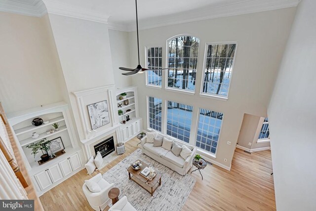 living room with ornamental molding, a towering ceiling, wood-type flooring, and built in features