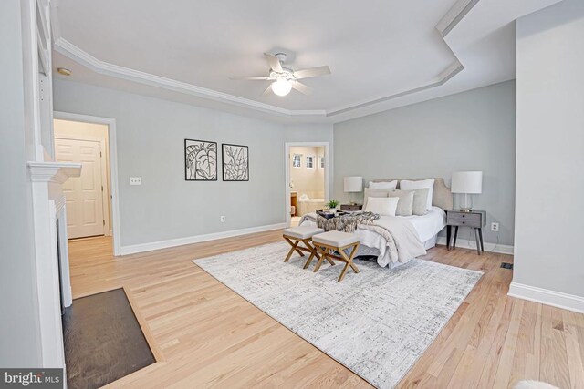 bedroom featuring ensuite bathroom, ceiling fan, light wood-type flooring, and a tray ceiling