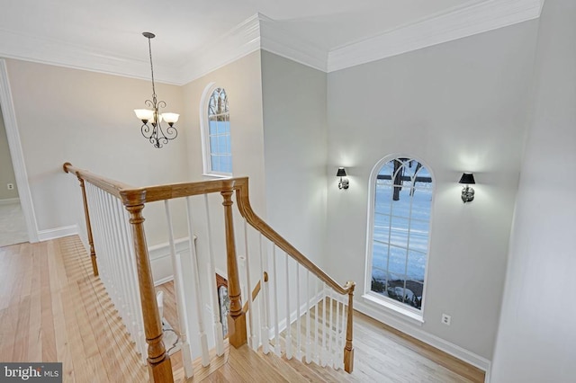 stairs with ornamental molding, wood-type flooring, and a chandelier