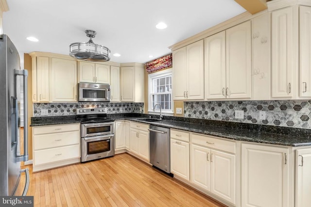 kitchen featuring sink, light hardwood / wood-style flooring, dark stone counters, stainless steel appliances, and cream cabinets