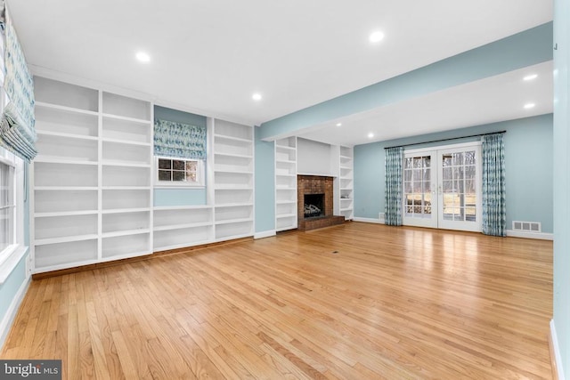 unfurnished living room with a brick fireplace, built in features, and light hardwood / wood-style floors