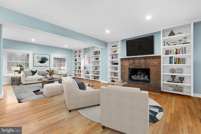 living room with built in features, a brick fireplace, and light hardwood / wood-style flooring