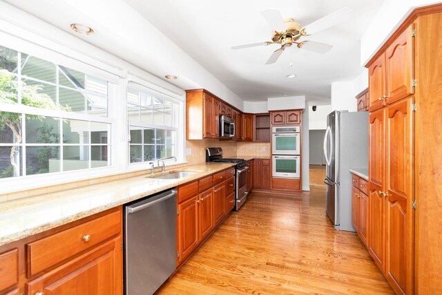 kitchen with sink, stainless steel appliances, light stone counters, tasteful backsplash, and light hardwood / wood-style floors