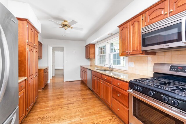 kitchen featuring sink, ceiling fan, appliances with stainless steel finishes, decorative backsplash, and light wood-type flooring