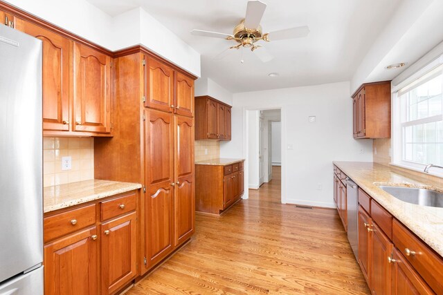 kitchen with appliances with stainless steel finishes, tasteful backsplash, sink, light stone countertops, and light wood-type flooring