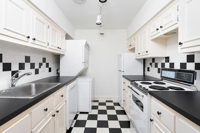 kitchen featuring sink, white appliances, stacked washer / dryer, tasteful backsplash, and white cabinets