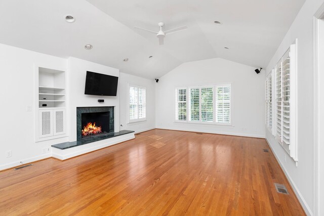 unfurnished living room with a premium fireplace, lofted ceiling, a healthy amount of sunlight, and built in features